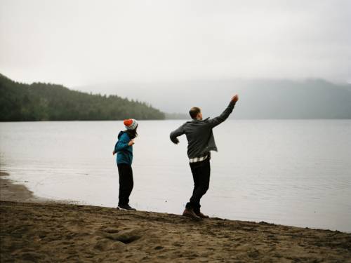 Ein 14jähriger Junge und ein Mann stehen am Wasserrand eines großen Gewässers. Es sieht aus, als werfen sie Steine ins Wasser.